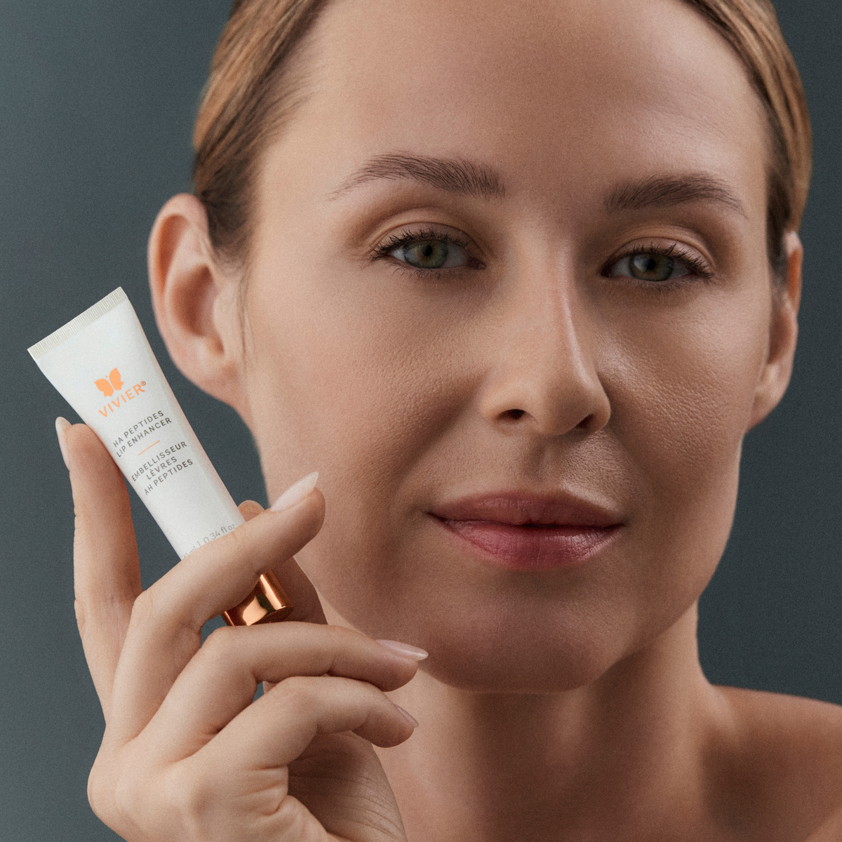 A close-up of a woman holding a white tube of Vivier HA Peptides Lip Enhancer now available at Foxy Face Studio in Orangeville, ON 