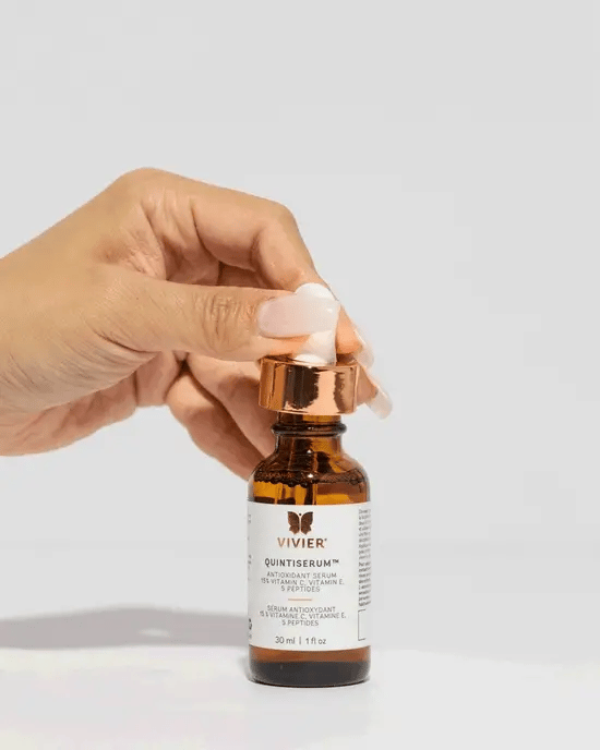 Hand pulling serum from bottle of Quintiserum -  Brightens and evens skin tone and texture